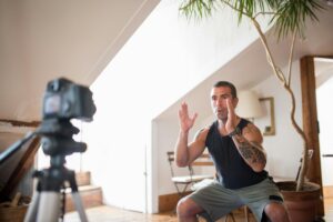 Tattooed man filming a workout video indoors, focusing on exercise technique.